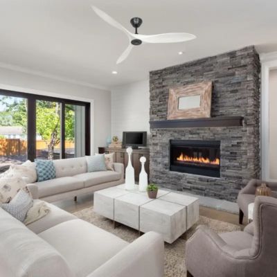 Comment équilibrer un ventilateur de plafond qui vacille : vue d’un salon moderne avec ventilateur au plafond et cheminée en pierre, canapé clair et grande baie vitrée.