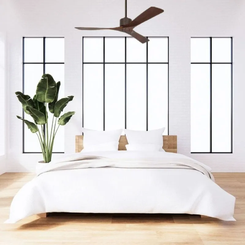 Chambre lumineuse avec lit blanc et végétal au côté, plafond ventilateur et grandes fenêtres noires.