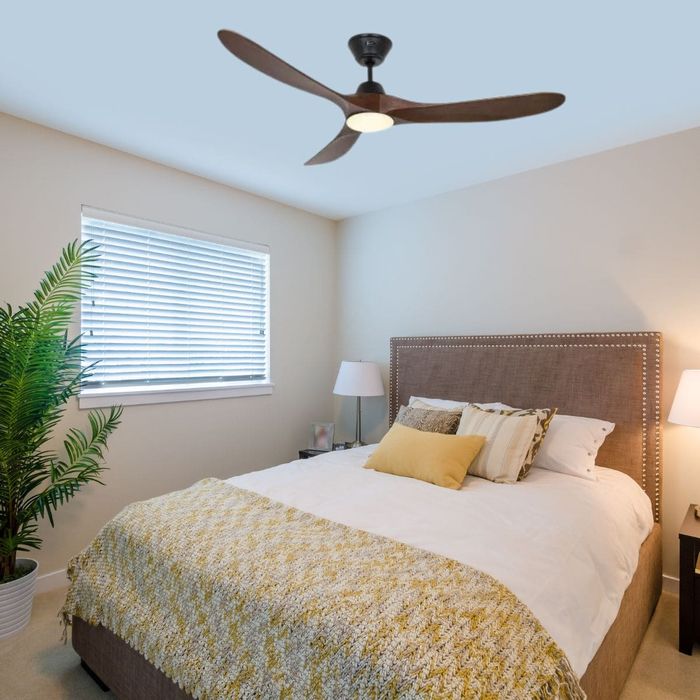 Lit double dans une chambre lumineuse avec ventilateur de plafond moderne au centre; plante en pot et lampes de chevet. Alt: "Lit double dans une chambre lumineuse avec ventilateur de plafond moderne."