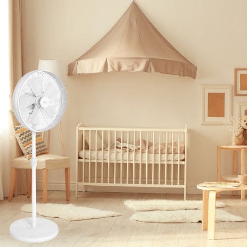 Ventilateur sur pied blanc dans une chambre près d’un lit à barreaux et d’un berceau.