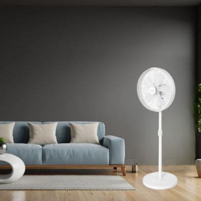 Ventilateur sur pied blanc debout dans un salon moderne devant un canapé gris.