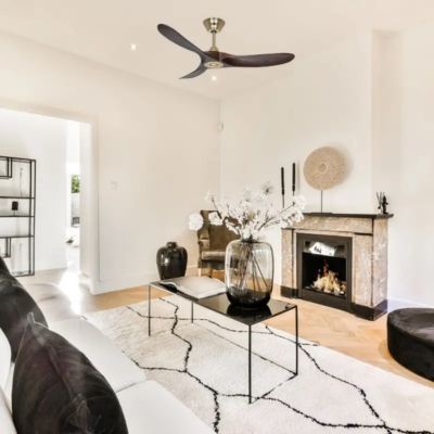 Ventilateur plafond basse consommation installé dans un salon lumineux avec cheminée, canapé blanc et décoration moderne.