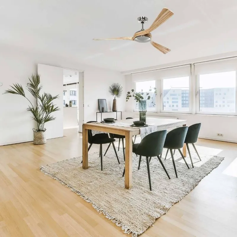Salle à manger lumineuse avec table en bois et six chaises noires sur un tapis clair.
