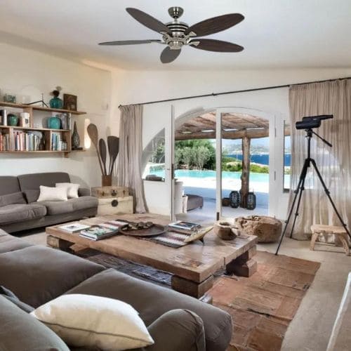 Salon lumineux avec canapé gris, table basse en bois et équipement de tournage en intérieur, vue sur l’extérieur par une