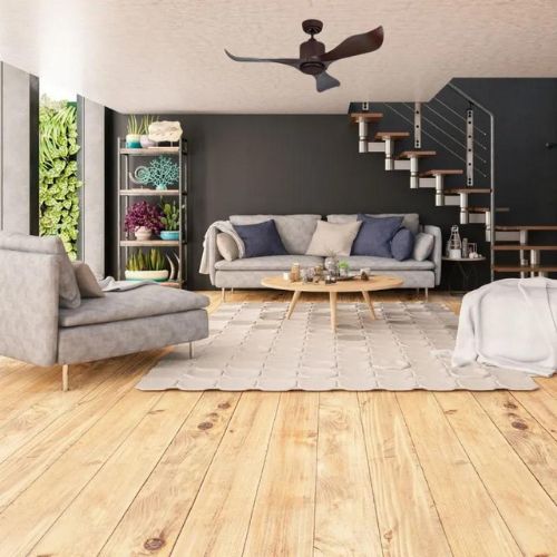 Salon lumineux avec canapés et fauteuils autour d’une table basse sur un tapis clair, sous un plafond avec un ventilateur et